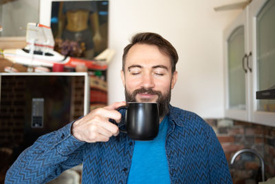 Handsome positive optimistic nice glad attractive guy holding cup of fresh coffee in kitchen