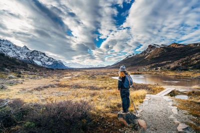 Woman standing on landscape against cloudy sky