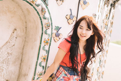 Portrait of beautiful young woman standing against wall