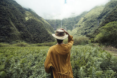 Rear view of woman wearing hat standing against cloudy sky in forest