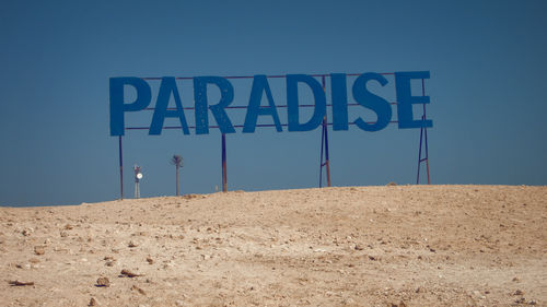 Information sign on beach against clear blue sky