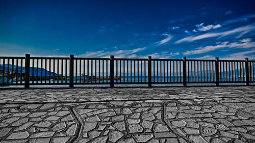 Empty footpath by railing against blue sky