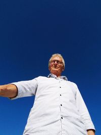 Low angle view of man walking against clear blue sky
