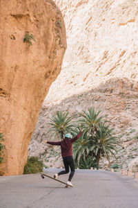 Rear view of woman skateboarding on road by mountains