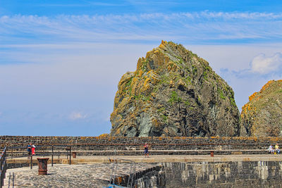 People on rock by sea against sky