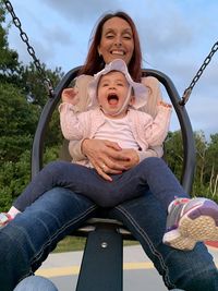 Low angle view of mother holding daughter sitting on swing