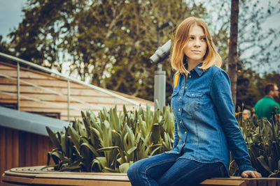 Woman sitting on bench against trees