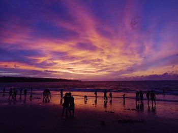 Silhouette people standing at beach against cloudy sky during sunset