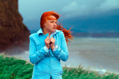 Young woman standing on field by sea