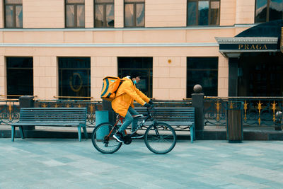 Rear view of man riding bicycle on street against building