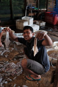 Portrait of smiling man holding cuttlefish fishes while crouching at fish market