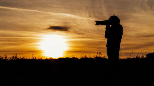 Silhouette man photographing on field against sky during sunset