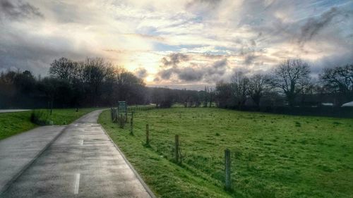 Road passing through grassy field against cloudy sky