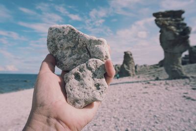 Midsection of person holding rock at beach against sky