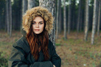 Young woman standing by tree trunk in forest