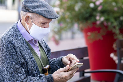 Active senior man using smart phone sitting on bench outdoors