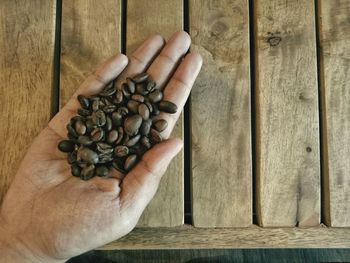 Close-up of human hand holding roasted coffee beans over table