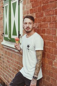 Man having ice cream while standing against brick wall