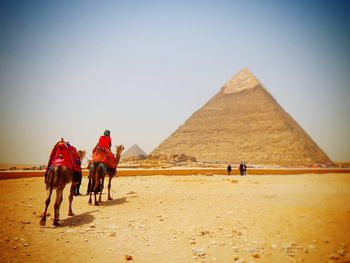 People riding horse on desert against sky