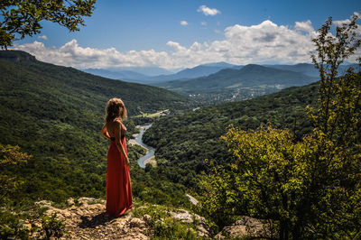 Full length of woman standing by cliff against landscape