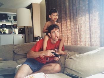 Shirtless boy with father playing video game at home