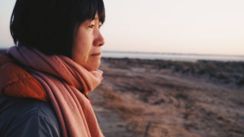 Side view of thoughtful mature woman looking away at beach against sky