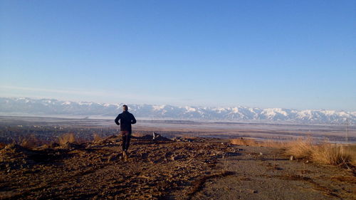 Rear view of man jogging on landscape against clear blue sky