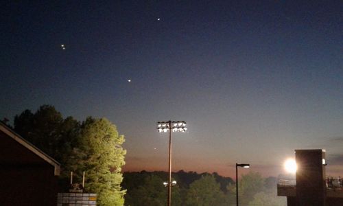 Illuminated street light by building against sky at night