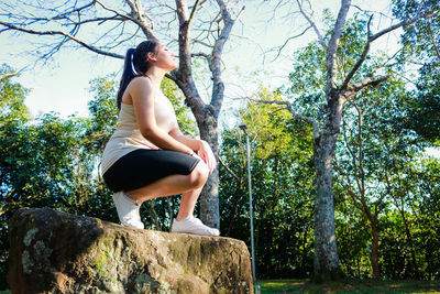 Low angle view of woman crouching on rock at park