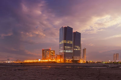 Illuminated buildings by sea against sky during sunset