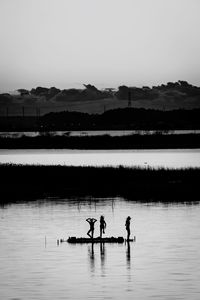 Silhouette people on lake against clear sky