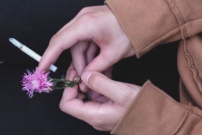 Cropped hands holding flower and cigarette over black background