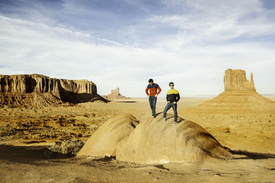 Friends standing on rock formations against sky