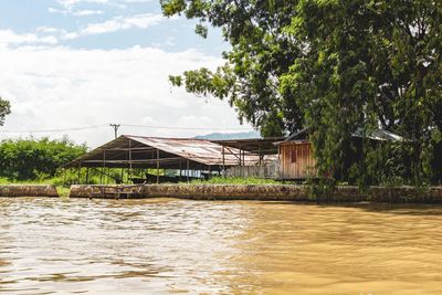 House by river and trees against sky