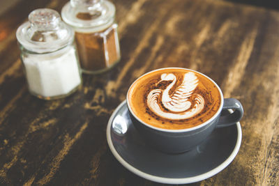 Cup of hot cappuccino on wooden table with latte art. there are two sugar cans