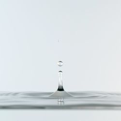Close-up of drop falling on water against white background