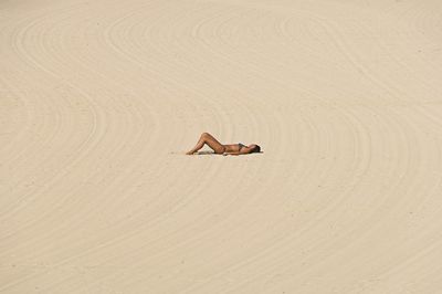 Side view of woman lying on sand at desert