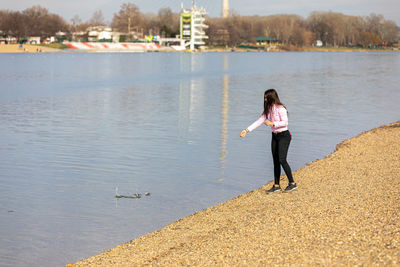 A young girl standing on the lake bank and throwing stones into the water. recreation in nature