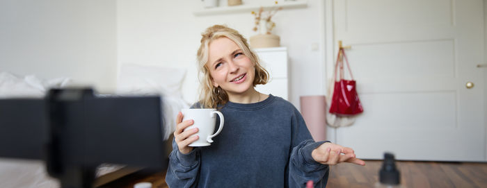 Portrait of smiling young woman standing against wall