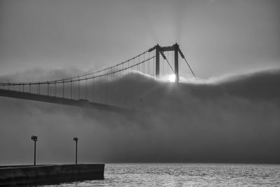 View of suspension bridge against cloudy sky and fog