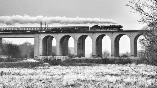 Low angle view of steam train on railway bridge against sky