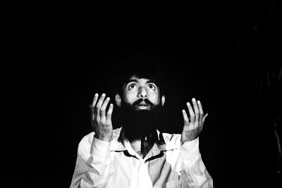 Portrait of young man standing against black background