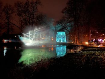 Illuminated city by lake against sky at night