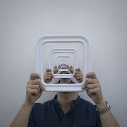 Multiple image of man holding blank picture frame against white wall