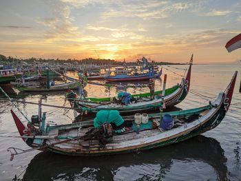 Fishing boats moored in sea against sky during sunset