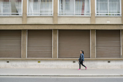 Full length of man walking on footpath against building