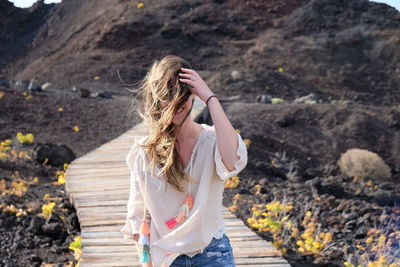 Young woman with tousled hair standing on boardwalk against mountain