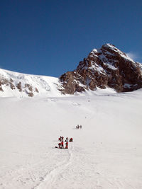 People on snowcapped mountain against clear sky during winter