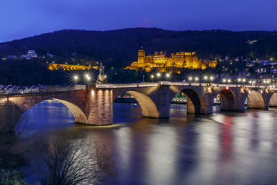 Illuminated bridge over river against sky at night