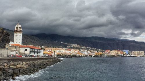 Town by river against cloudy sky